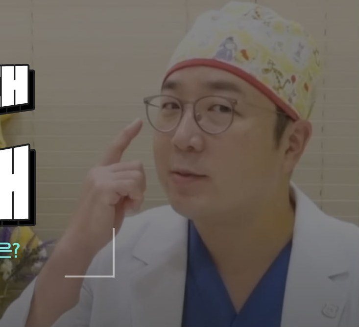 수술모자를 쓰고 손가락으로 광대 부위를 가리키며 설명하는 의사