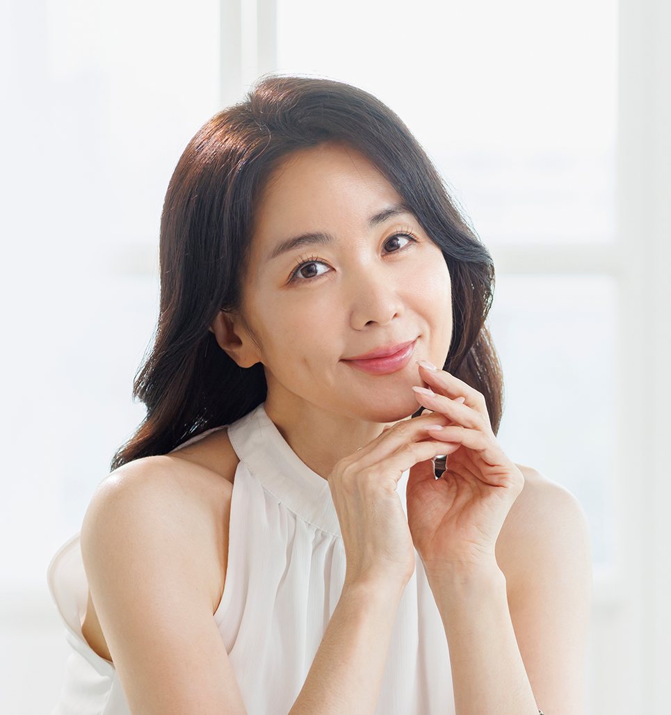 흰 민소매 블라우스 차림으로 턱 아래 두 손을 모은 중년 여성 모델