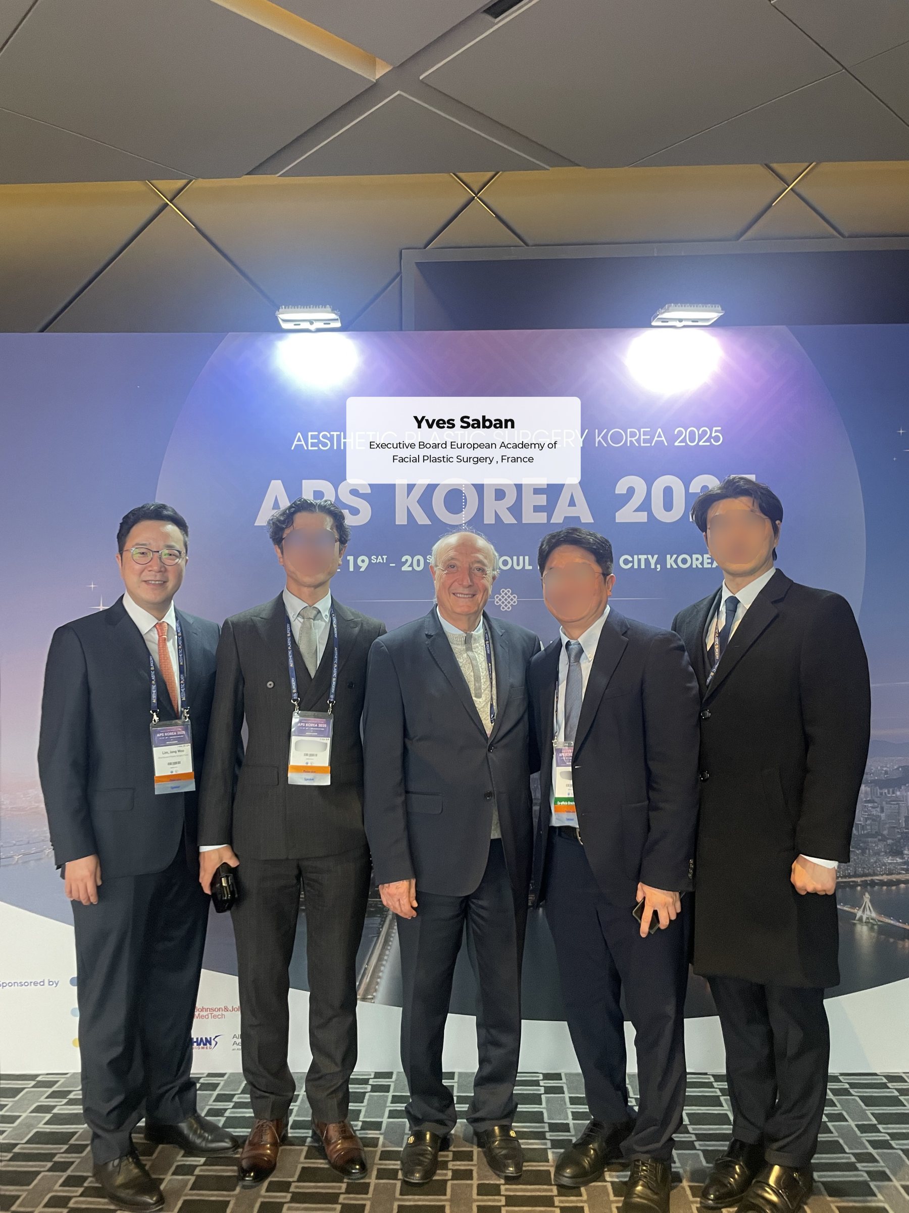 APS KOREA 2025 포토월 앞 단체 사진 — 'Yves Saban, Executive Board European Academy of Facial Plastic Surgery, France' 표기(다른 의료진 얼굴 흐림 처리)