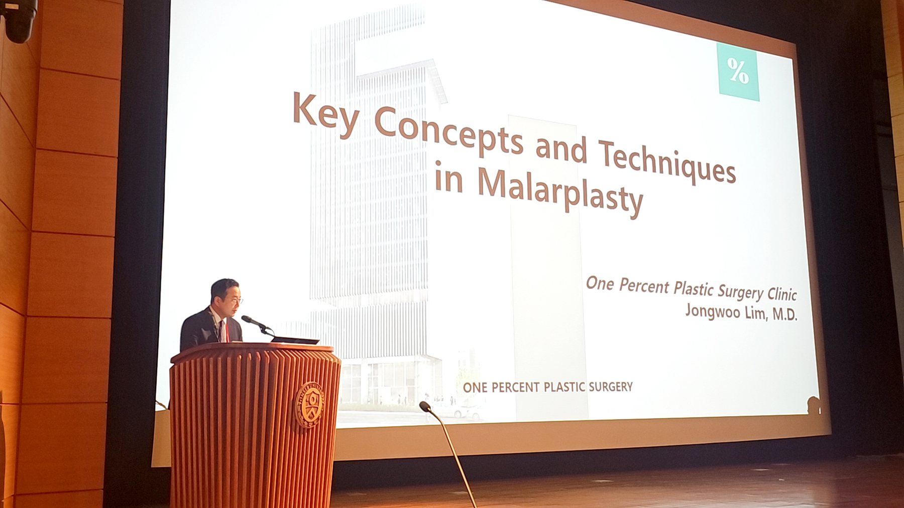 ‘Key Concepts and Techniques in Malarplasty’ 슬라이드 앞 연단에서 강연하는 임종우 대표원장